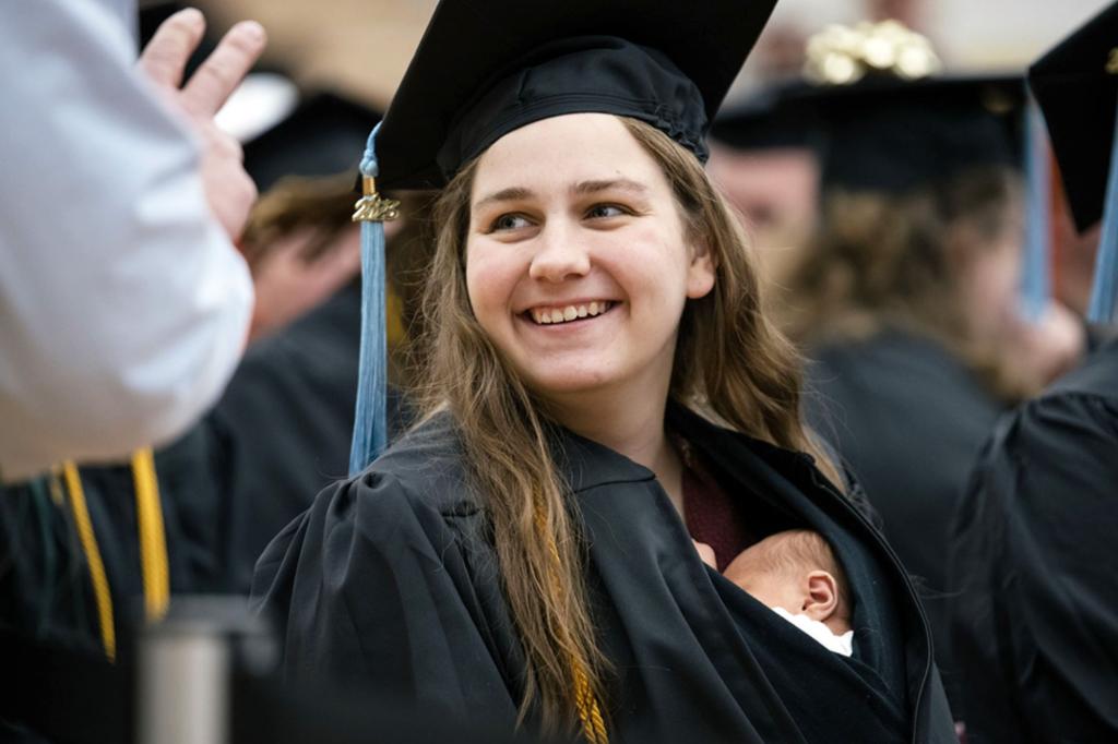امرأة من ميشيغان تمشي على خشبة المسرح في حفل التخرج الجامعي مع ابنتها البالغة من العمر 10 أيام داخل ثوبها