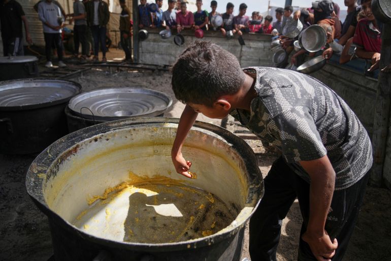 A boy scrapes leftovers from an empty pot after all the meals were distributed at a community kitchen in Khan Younis, southern Gaza Strip, Wednesday, May 14, 2025. (AP Photo/Abdel Kareem Hana)